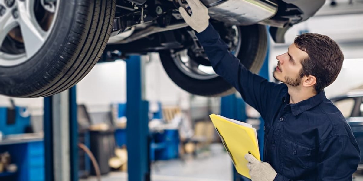 mechanic-inspecting-the-under-side-of-a-car-with-a-clipboard